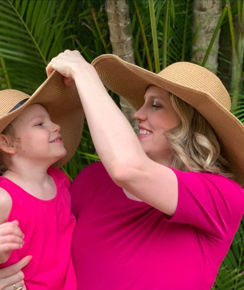 Holly smiles and adjust her daughter Maggie's hat. Both wear matching sunhats and pink shirts