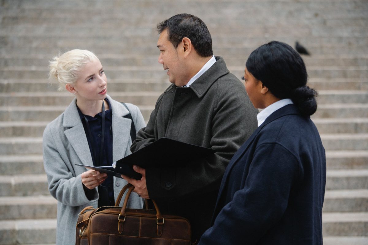 Three people in suits,stand on the marble steps of a government building, talking about the content in a black binder.