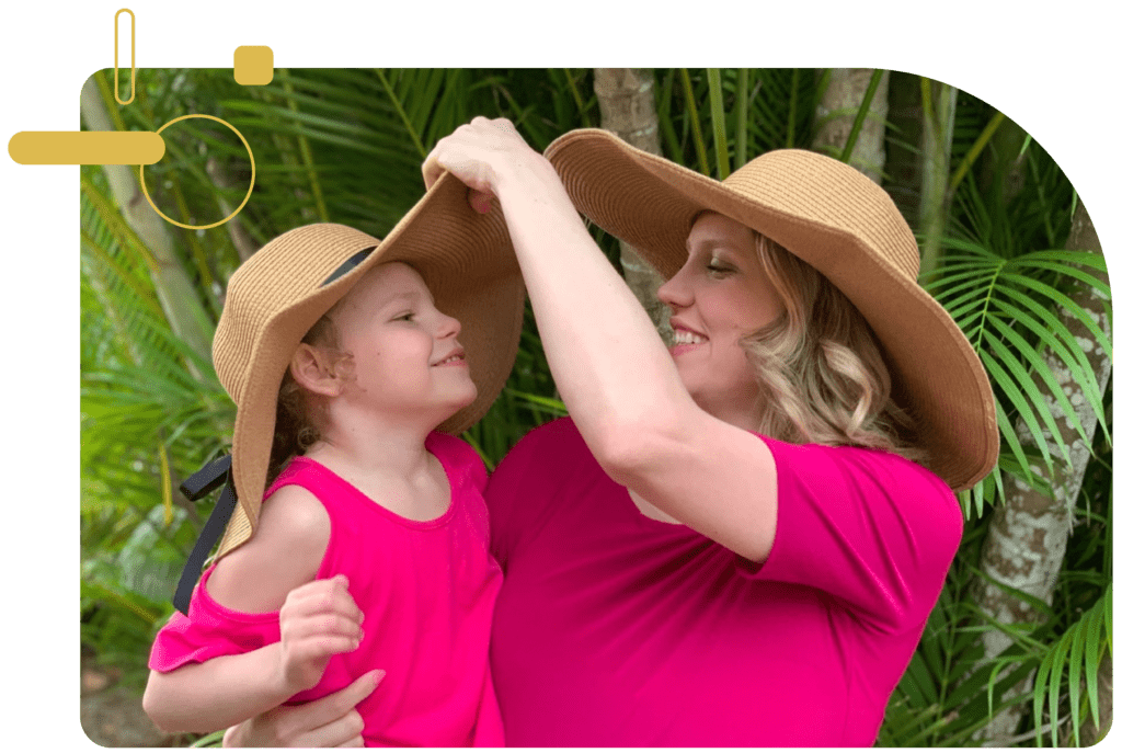 Holly smiles and adjust her daughter Maggie's hat. Both wear matching sunhats and pink shirts