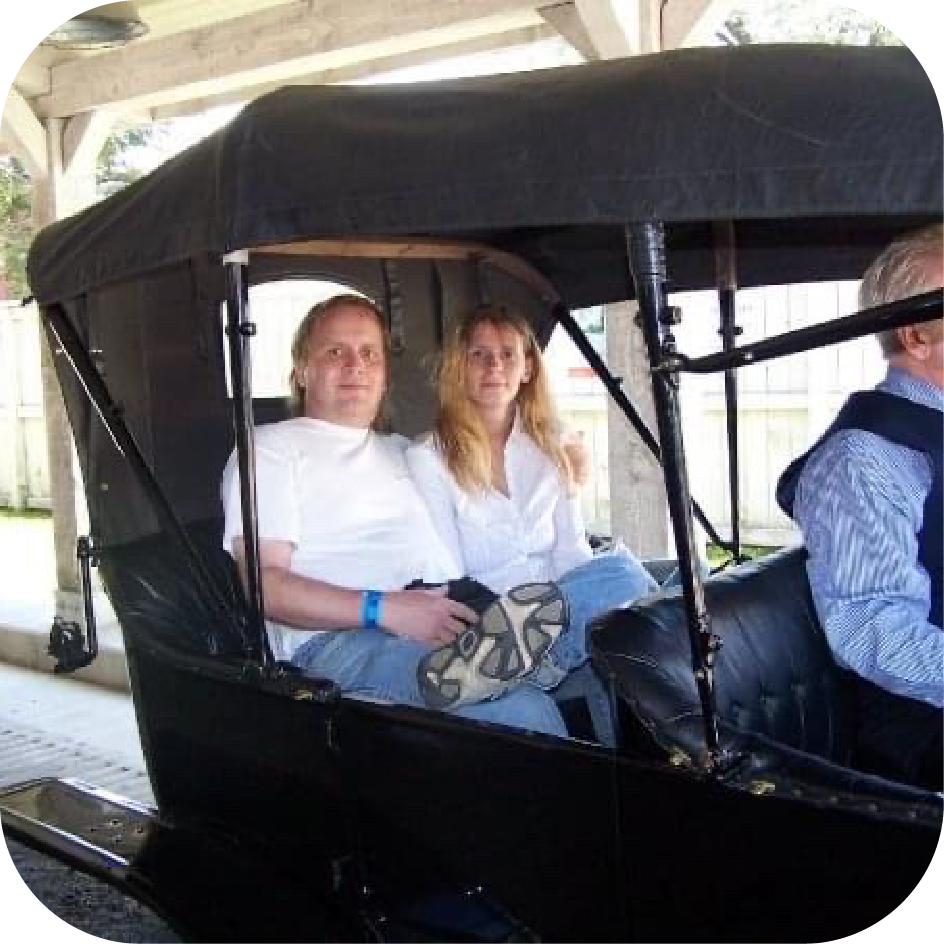 Dave and Kathy are sitting together in the back of a vintage buggy. Off-screen is the horse and driver. They're both smiling at the camera.