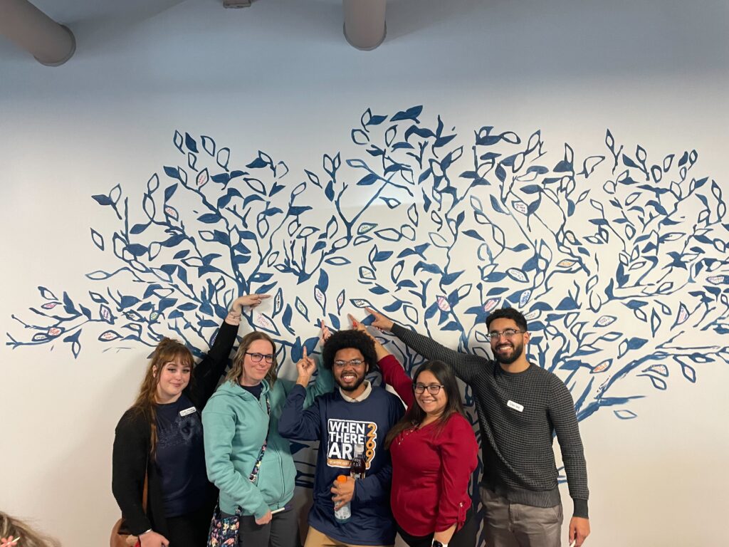 GT employees smile and point at a mural where they have signed their names as a leaf in a tree.